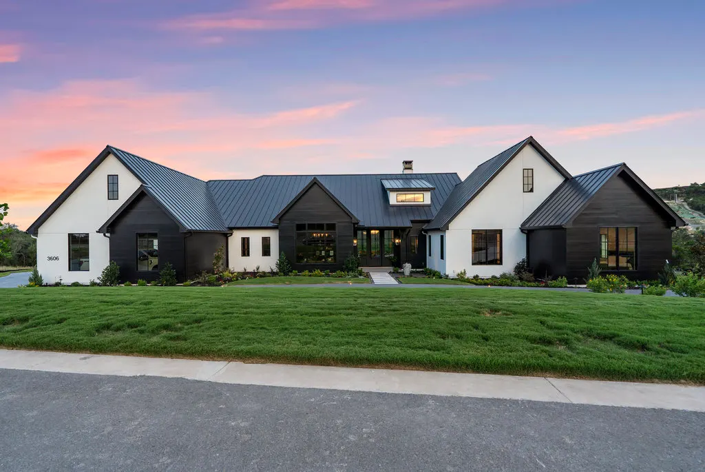 A low modern home in black and white across a Hill Country lawn at dusk