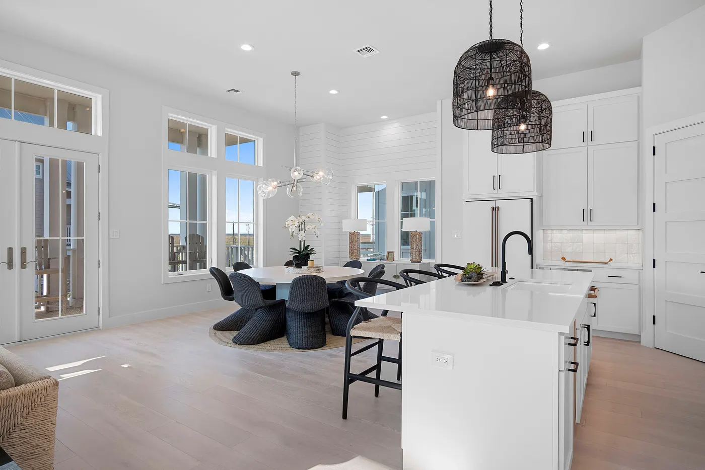A white modern kitchen with black-framed pendants and dining beyond